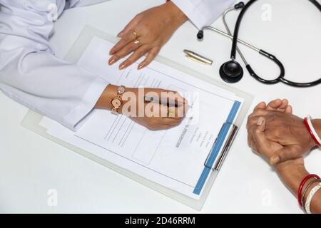 Indische Ärztin schreibt ein Rezept, während ein Patient wartet Mit gepackten Händen in einer Klinik` Stockfoto